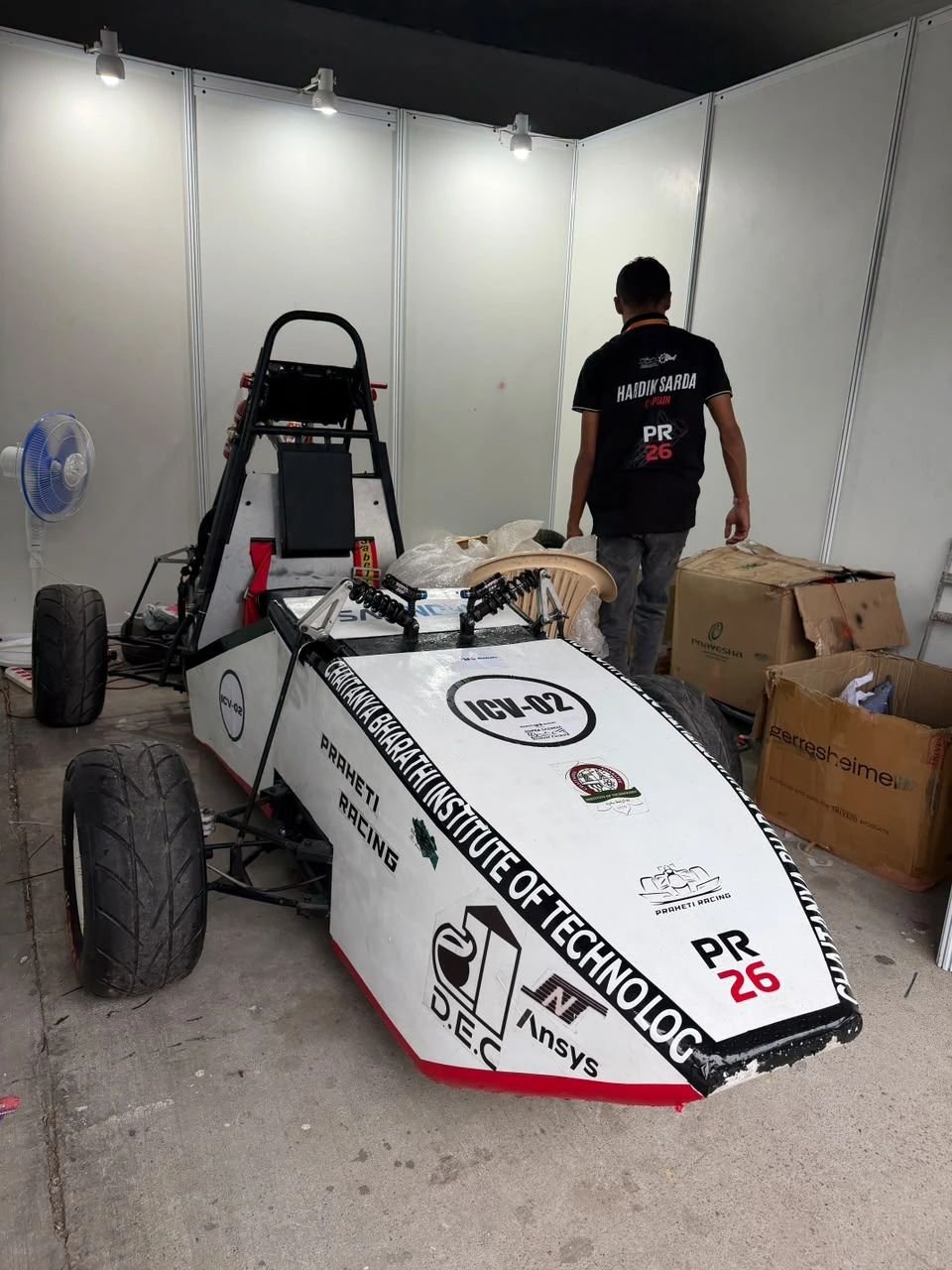 Praheti Racing PR26 Formula Student car, number ICV-02, in the pit box at SUPRA SAEINDIA 2026, with Hardik Sarda in his captain's team shirt